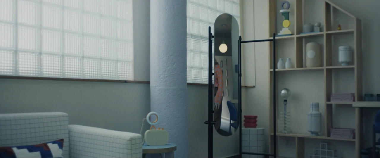 Sign Here (2017) movie still: medium — A minimalist living room features a white grid-patterned sofa and light wood shelving. A freestanding mirror…
