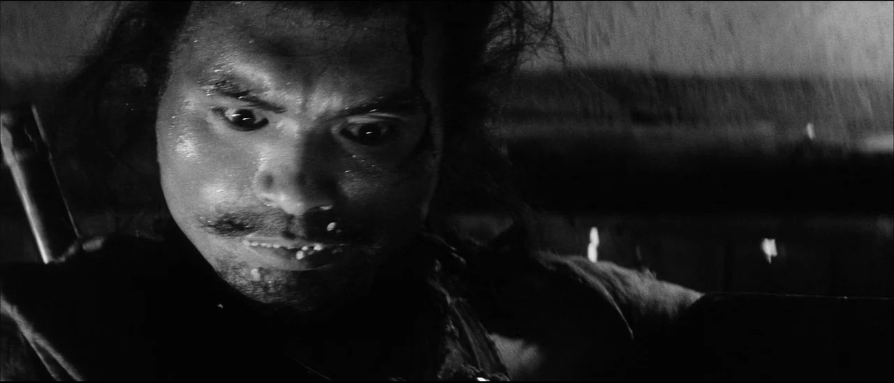 Kuroneko (1968) movie still: closeup — An outdoor location during a rainstorm at night with limited ambient light. A man with wild hair stares…