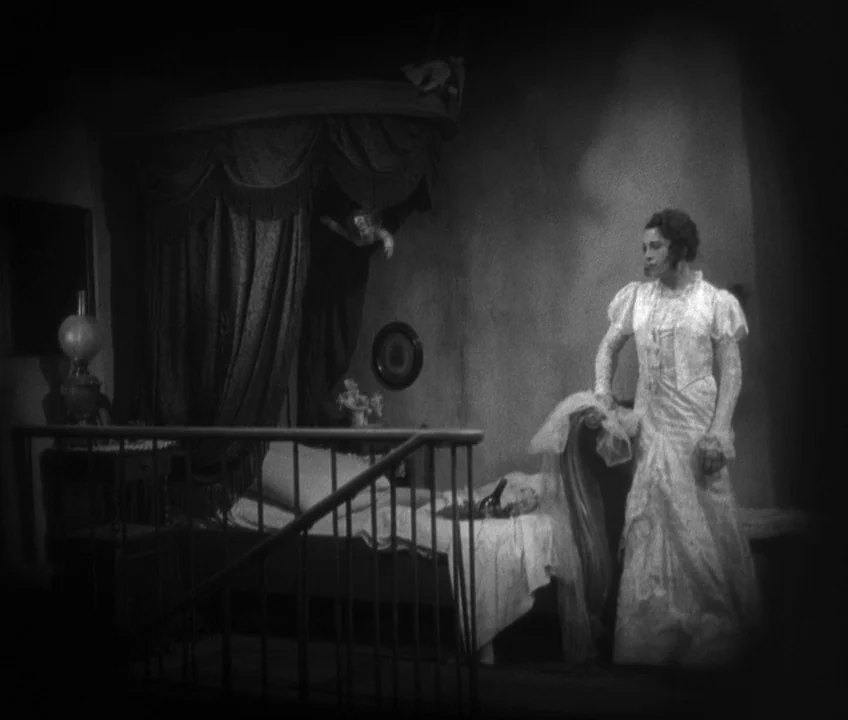 The Threepenny Opera (1931) movie still: fullbody — A dimly lit room contains a draped bed with a canopy and a small lamp. A woman wearing a long…