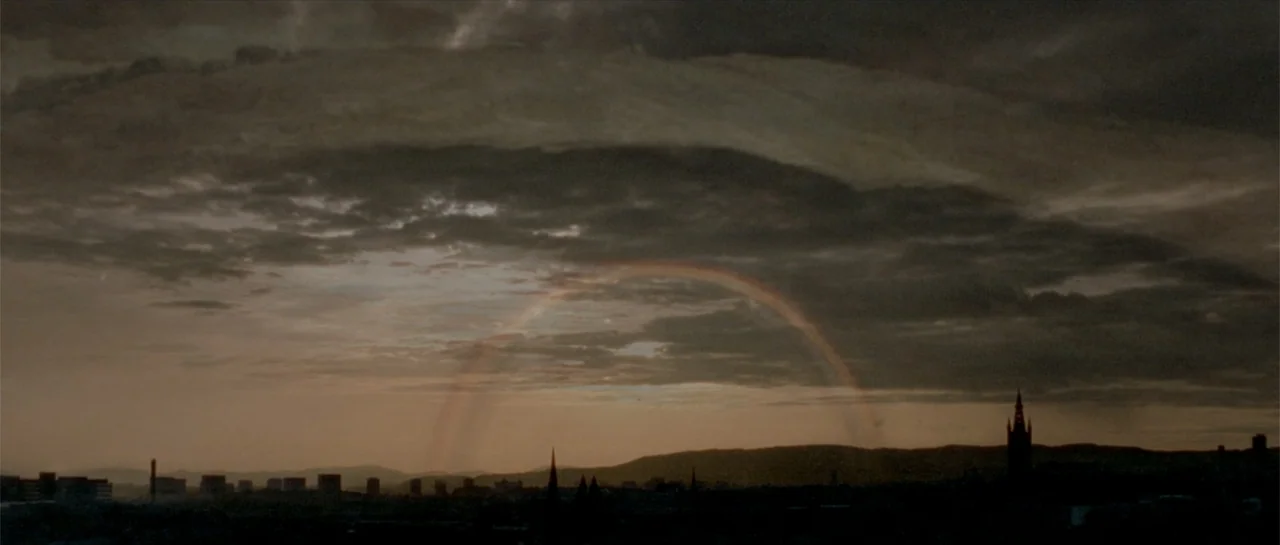 Breaking the Waves (1996) movie still: establishing — A distant silhouette of a city with church spires sits beneath heavy evening clouds. A thin,…