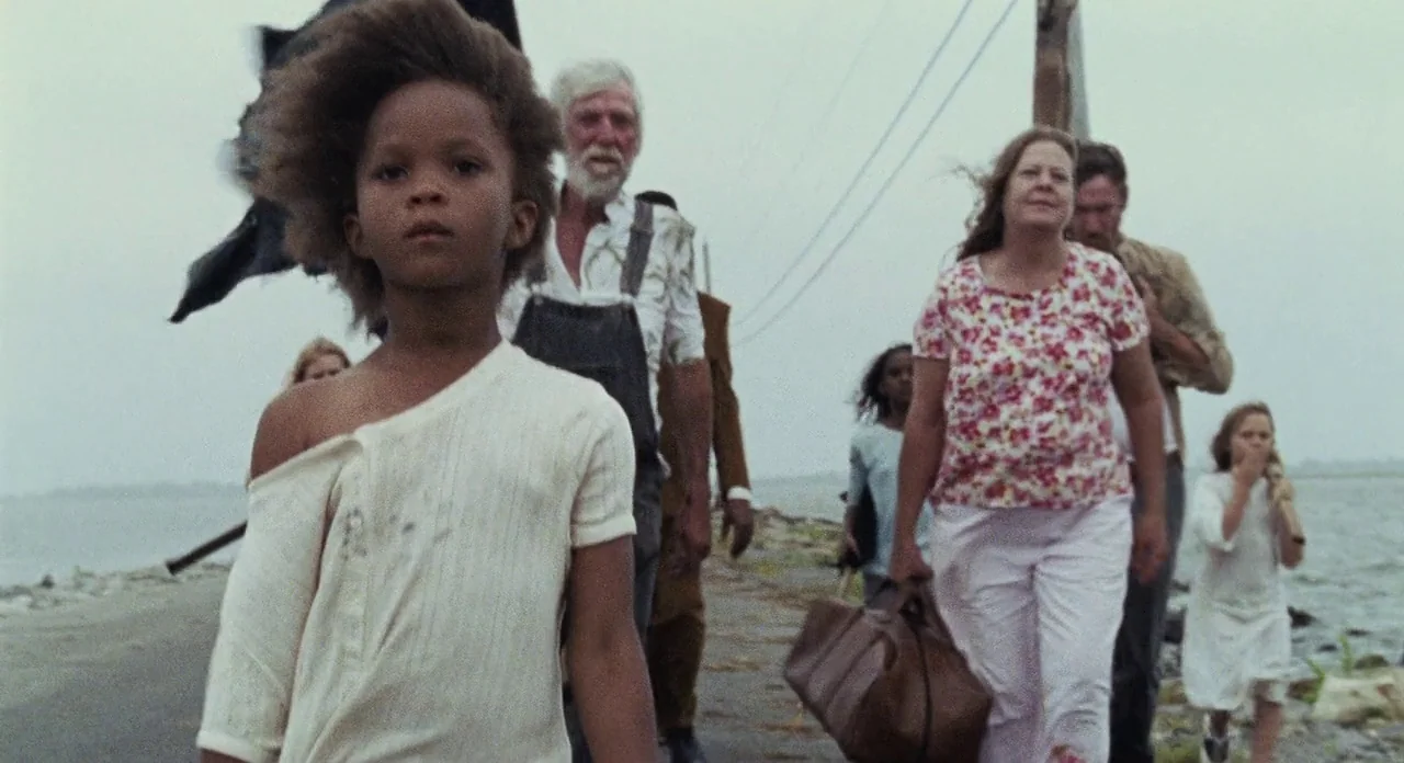 Beasts Of The Southern Wild (2012) movie still: medium — A group of people walk along a narrow, weathered concrete path beside the water. They carry…