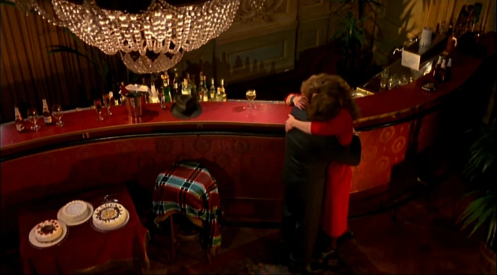 Wings Of Desire (1987) movie still: wide — A dimly lit, high-end bar features red wall panels and a large crystal chandelier. A man and a woman in…