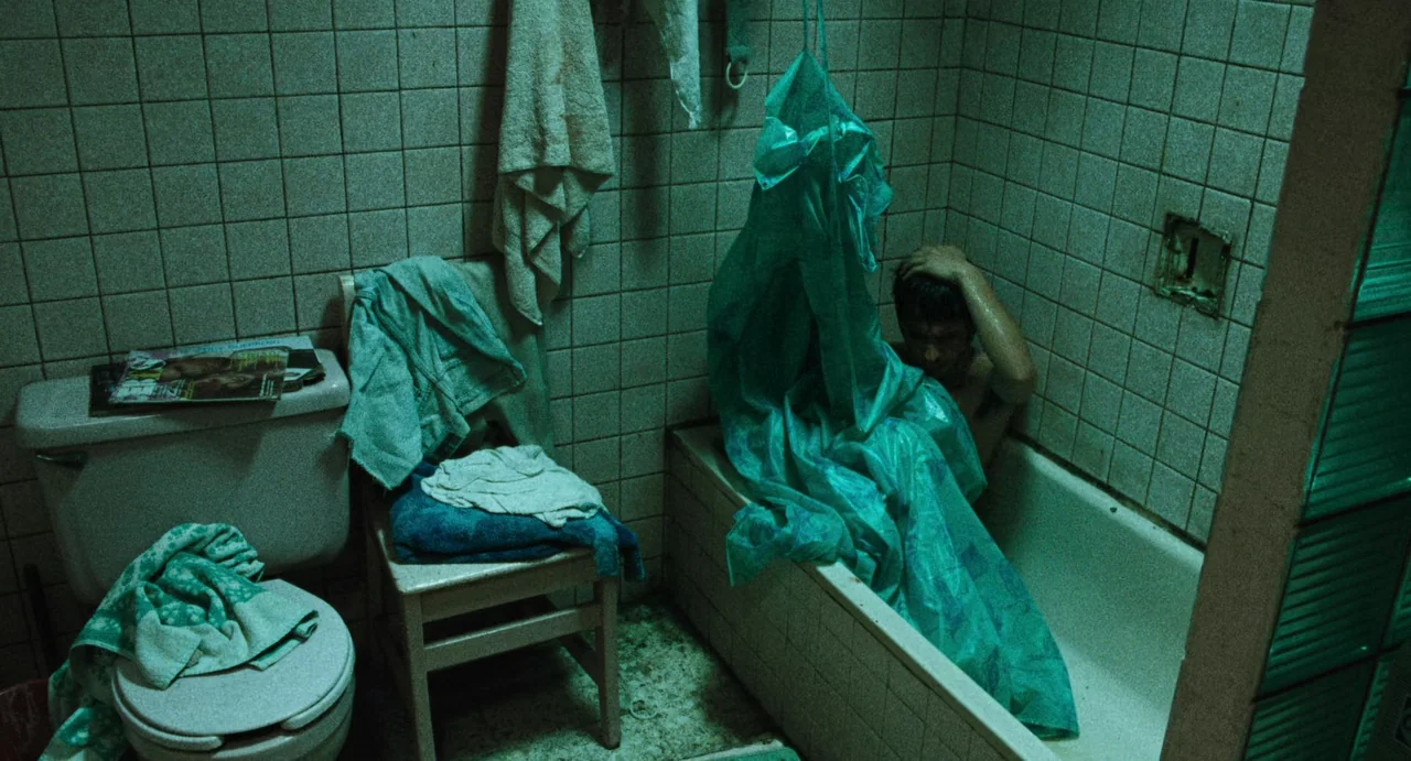 Amores Perros (2000) movie still: medium — A tiled room contains a bathtub, a toilet, and a small wooden chair. A shirtless man sits hunched over in…