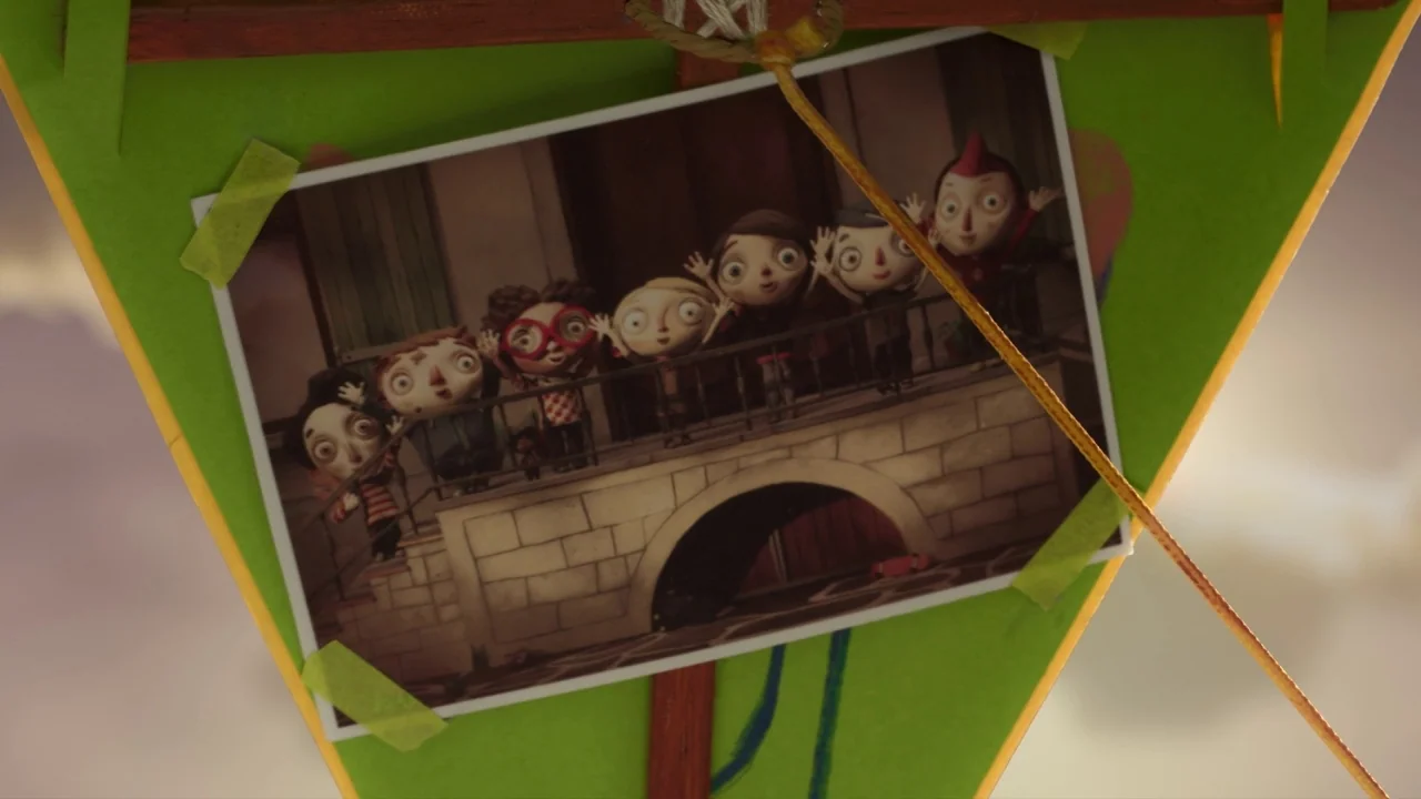 My Life as a Zucchini (2016) movie still: closeup — A green paper kite holds a photograph of six animated children on a bridge. The kite frame is…