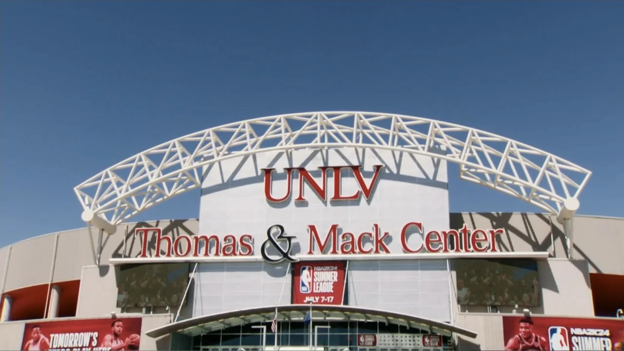 We Beat the Dream Team (2025) movie still: establishing — The exterior facade of the Thomas and Mack Center at UNLV under clear skies. A white…