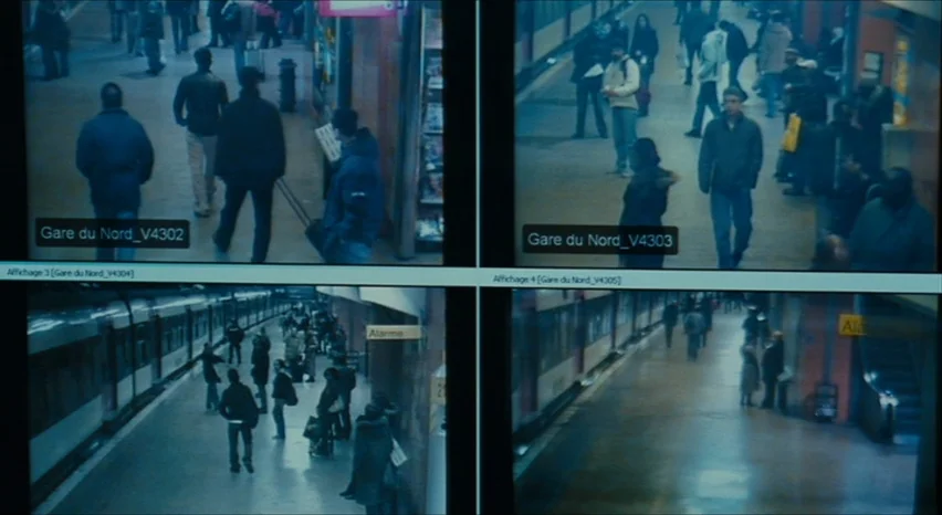 35 Shots of Rum (2008) movie still: wide — Four separate video feeds show a busy train station platform with commuters walking around. The monitors…