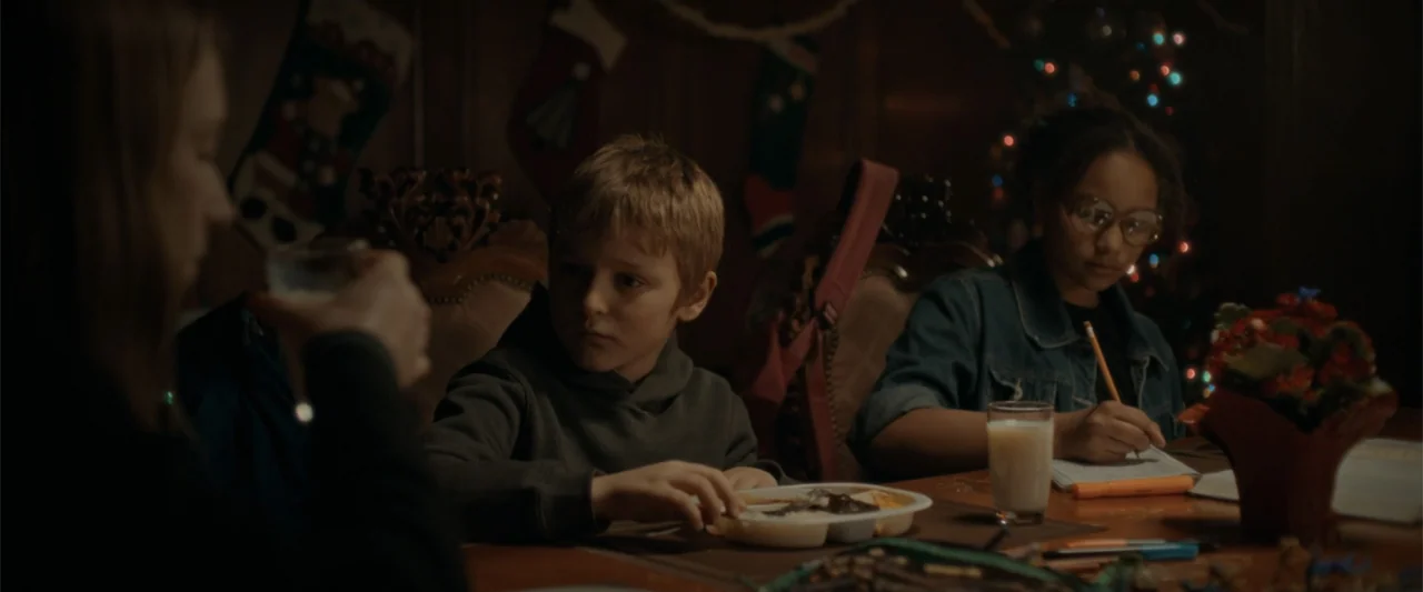 Silent Night, Deadly Night (2025) movie still: medium — A dimly lit dining room features wood-paneled walls decorated with hanging Christmas…