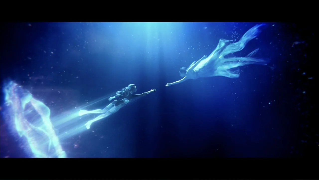 Lee Soo Man: King of K-Pop (2025) movie still: wide — An expanse of deep blue ocean water illuminated by shafts of light from above. Two women swim…