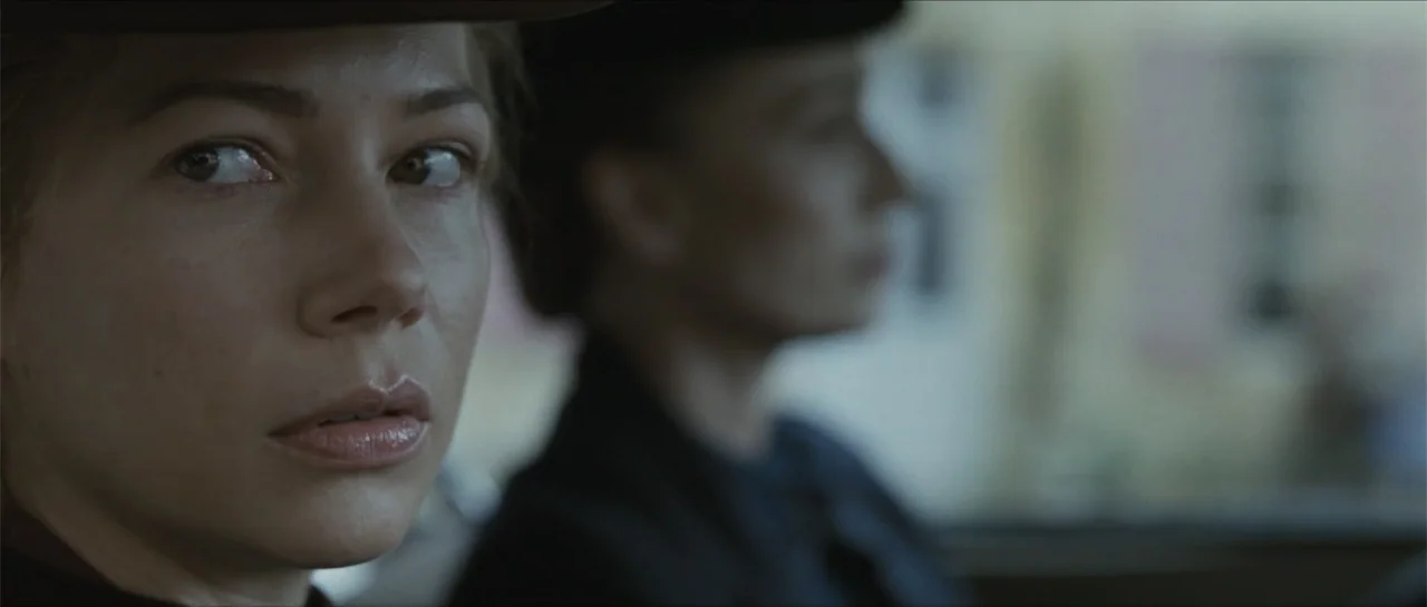 Suite Française (2015) movie still: closeup — The interior of a vintage automobile with a woman in the foreground and a blurred driver. The woman…