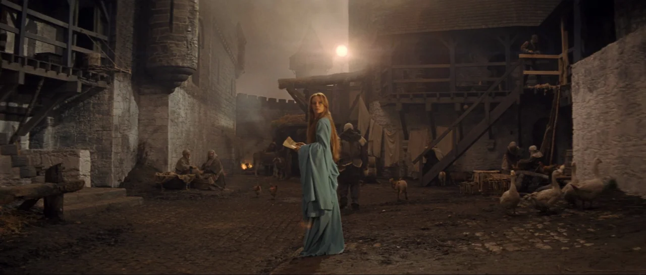 Macbeth (1971) movie still: fullbody — A stone-walled courtyard in a medieval setting features wooden scaffolds and dirt ground. A woman in a long…