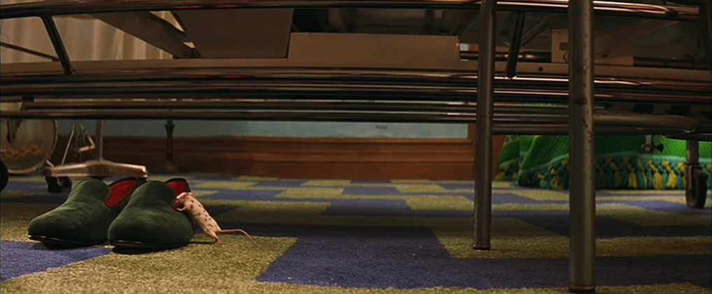 The Royal Tenenbaums (2001) movie still: wide — The underside of a metal bed frame sits on a patterned blue and green carpet. A single small mouse…