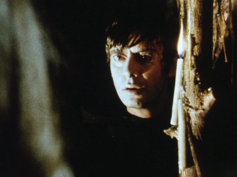 Our Lady of the Turks (1968) movie still: closeup — A dark rocky cavern interior features a man lit by a nearby candle. The man looks toward the…