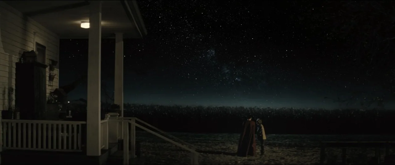 Batman v Superman: Dawn of Justice (2016) movie still: wide — A dimly lit wooden farmhouse porch overlooks a vast, dark rural field at night. Two…