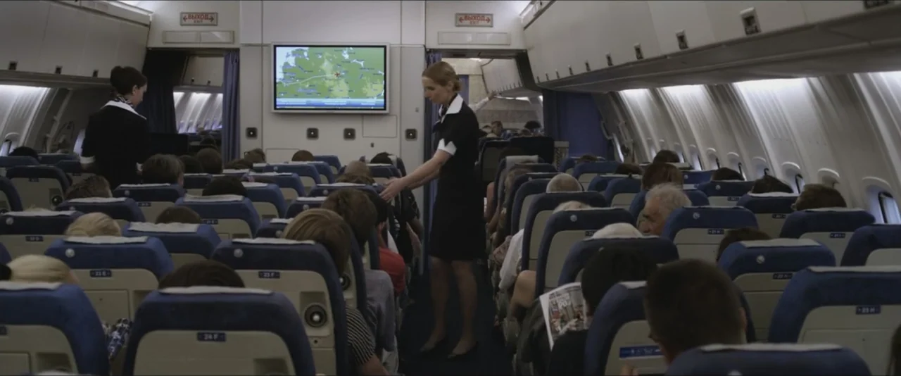 Darkest Hour (2017) movie still: medium — The interior of a commercial airplane cabin features rows of blue seats and overhead bins. A flight…