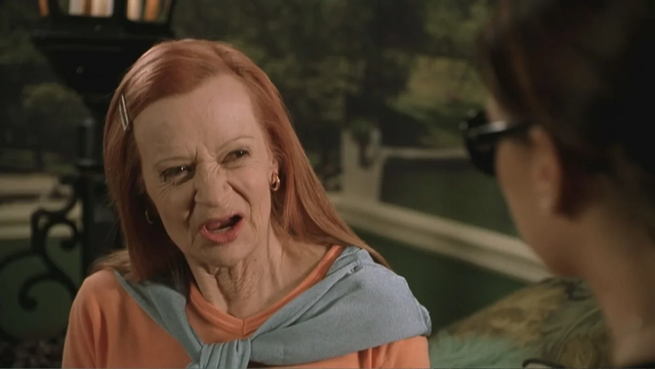 Not Another Teen Movie (2001) movie still: medium — An outdoor patio setting with blurred greenery in the background. An elderly woman with red hair…