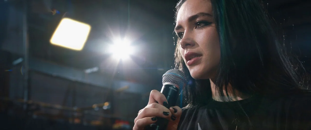 Fighting With My Family (2019) movie still: closeup — A dark, industrial indoor space features a bright spotlight behind the main subject. The woman…