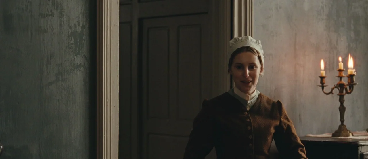 Madame Bovary movie still: medium — A dimly lit interior space with textured dark walls and a doorway. A young woman in period clothing stands in…