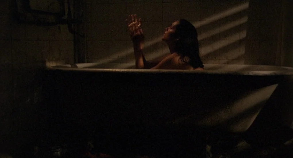Furia (1999) movie still: medium — A dimly lit room features a white claw-foot bathtub against tiled walls. A woman is partially visible while…