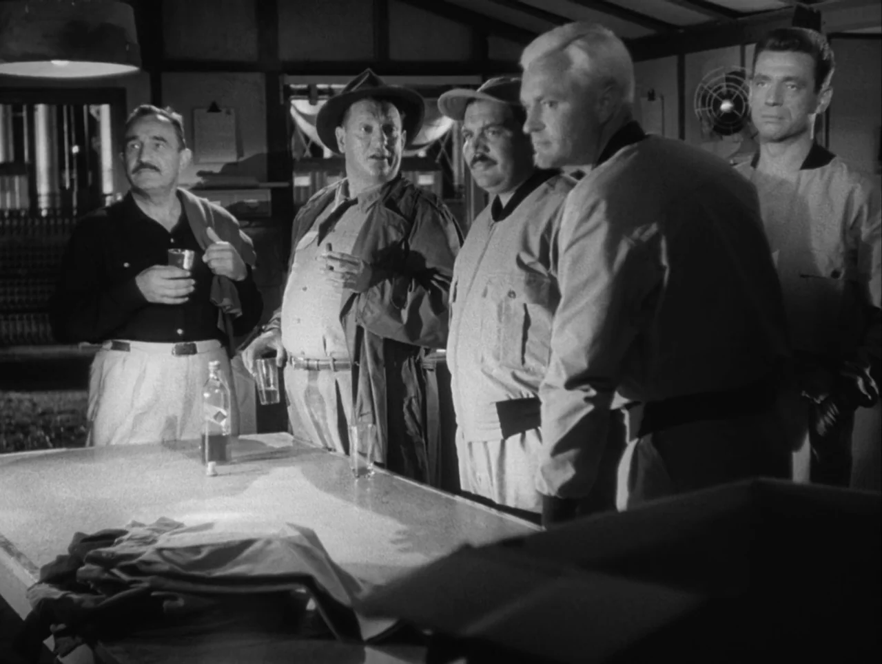 The Wages of Fear (1953) movie still: medium — An interior space features wood-paneled walls and exposed ceiling beams. Five men stand together…