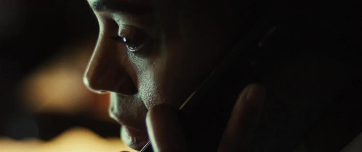 Emilia Pérez (2024) movie still: closeup — A dark vehicle interior at night with minimal ambient light sources. A person holds a mobile phone…