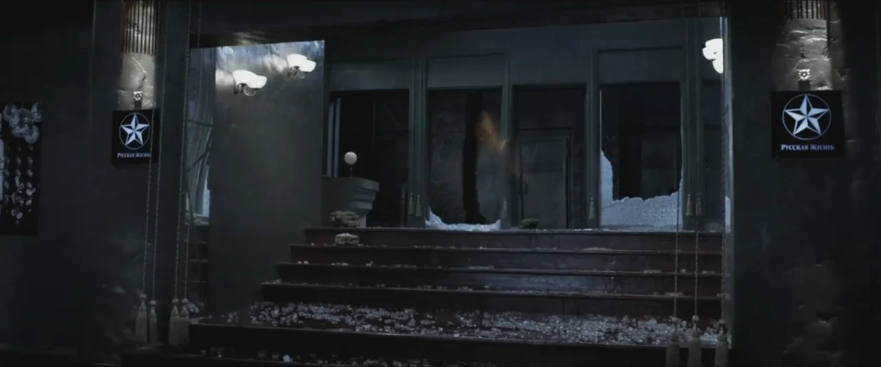 Darkest Hour (2017) movie still: establishing — A dark building exterior features a set of stairs leading to a shattered entrance. Glass shards are…