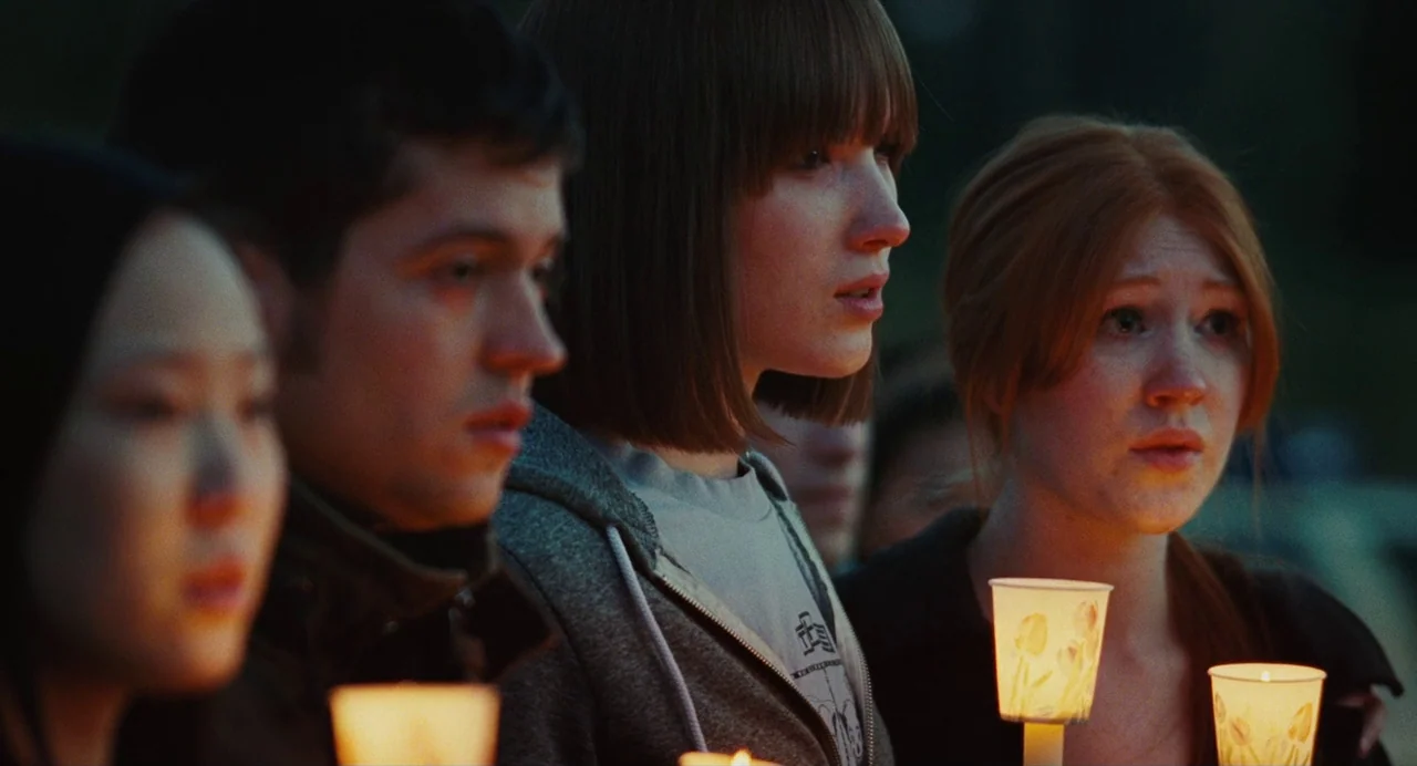 Jennifer’s Body (2009) movie still: medium — A diverse group of young adults stand together in a dark, outdoor setting. They each hold a lit candle…