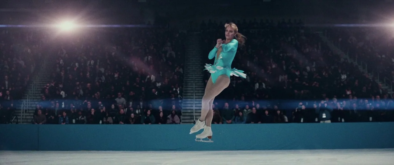 I, Tonya (2017) movie still: fullbody — A large indoor ice rink filled with a seated audience in dim stadium lighting. A female figure skater in a…