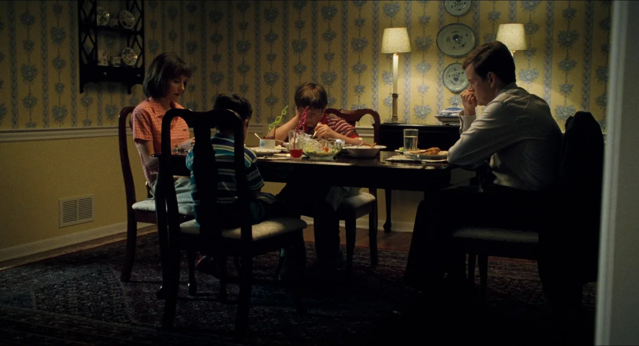 Happiness (1998) movie still: medium — A dark dining room with yellow floral wallpaper and a dark wood table. A father, mother, and two children sit…