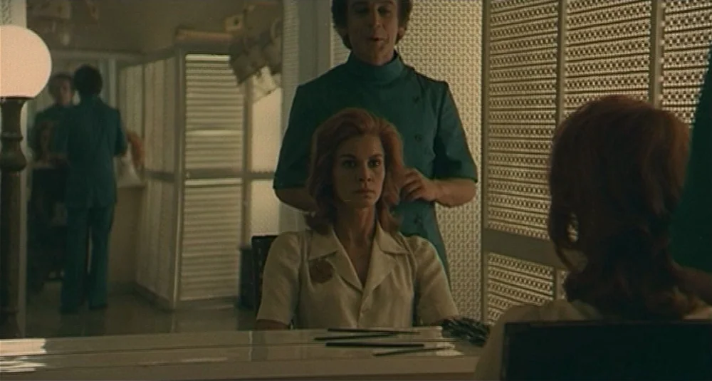 Footprints (Le Orme) (1975) movie still: medium — A sterile professional salon with partitioned walls and a large vanity mirror. A woman sits in a…
