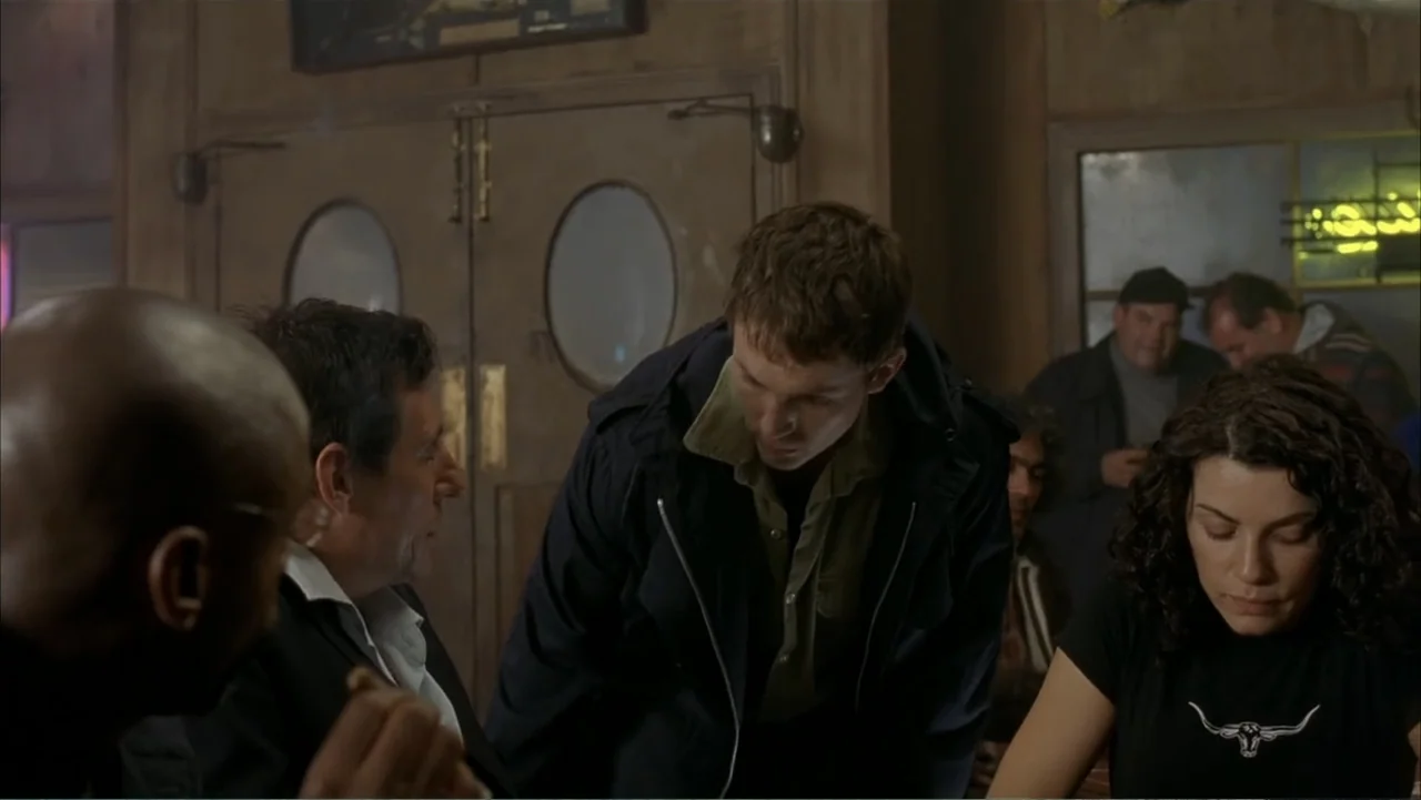Ghost Ship (2002) movie still: medium — A dimly lit bar interior features wooden paneled walls and vintage circular doors. A group of adults gathers…