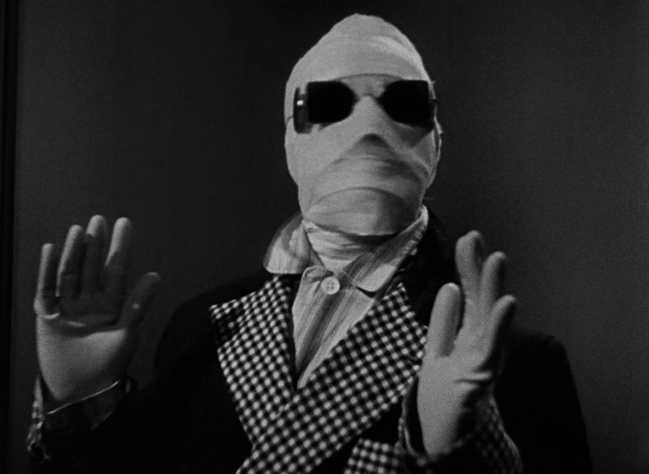 The Invisible Man (1933) (1933) movie still: medium — A figure stands in a dark room with minimal architectural features visible. The character…
