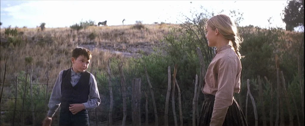 There Will Be Blood (2007) movie still: medium — A rural landscape features a young boy and girl separated by a wooden fence. The setting is a dry,…