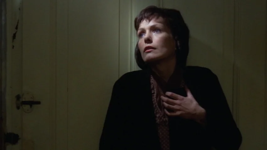 Tenderness of the Wolves (1973) movie still: medium — A woman stands indoors leaning against a plain wall next to a wooden door. She has her hand…