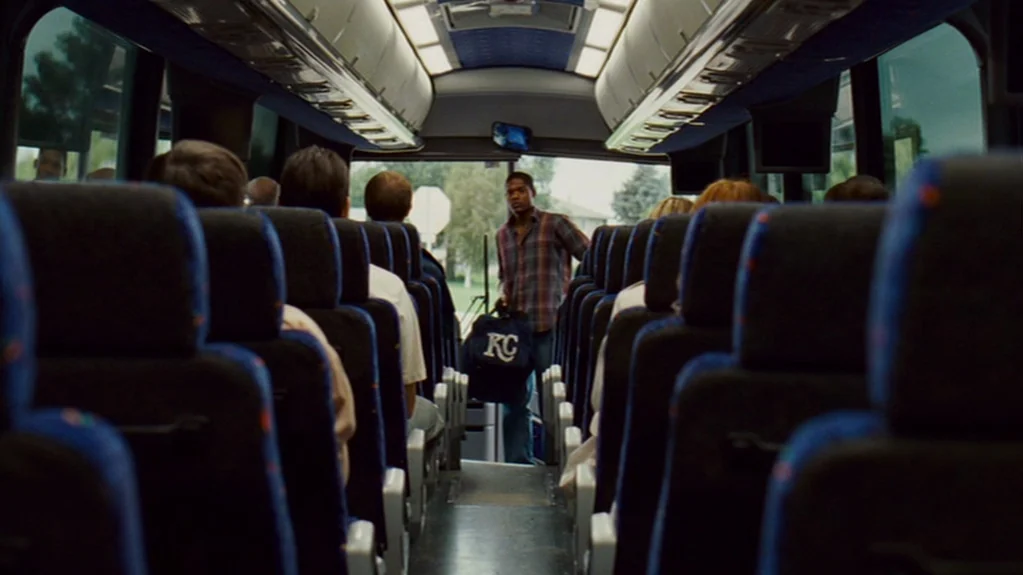 Sugar (2008) movie still: medium — The interior of a passenger bus with blue fabric seats lining the aisle. A young man stands near the exit holding…