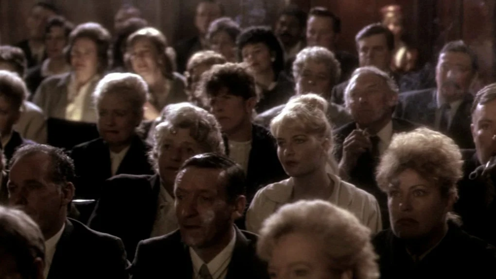 Distant Voices, Still Lives (1988) movie still: medium — A crowded audience sits in a dark, wood-paneled theater hall. People watch intently while…