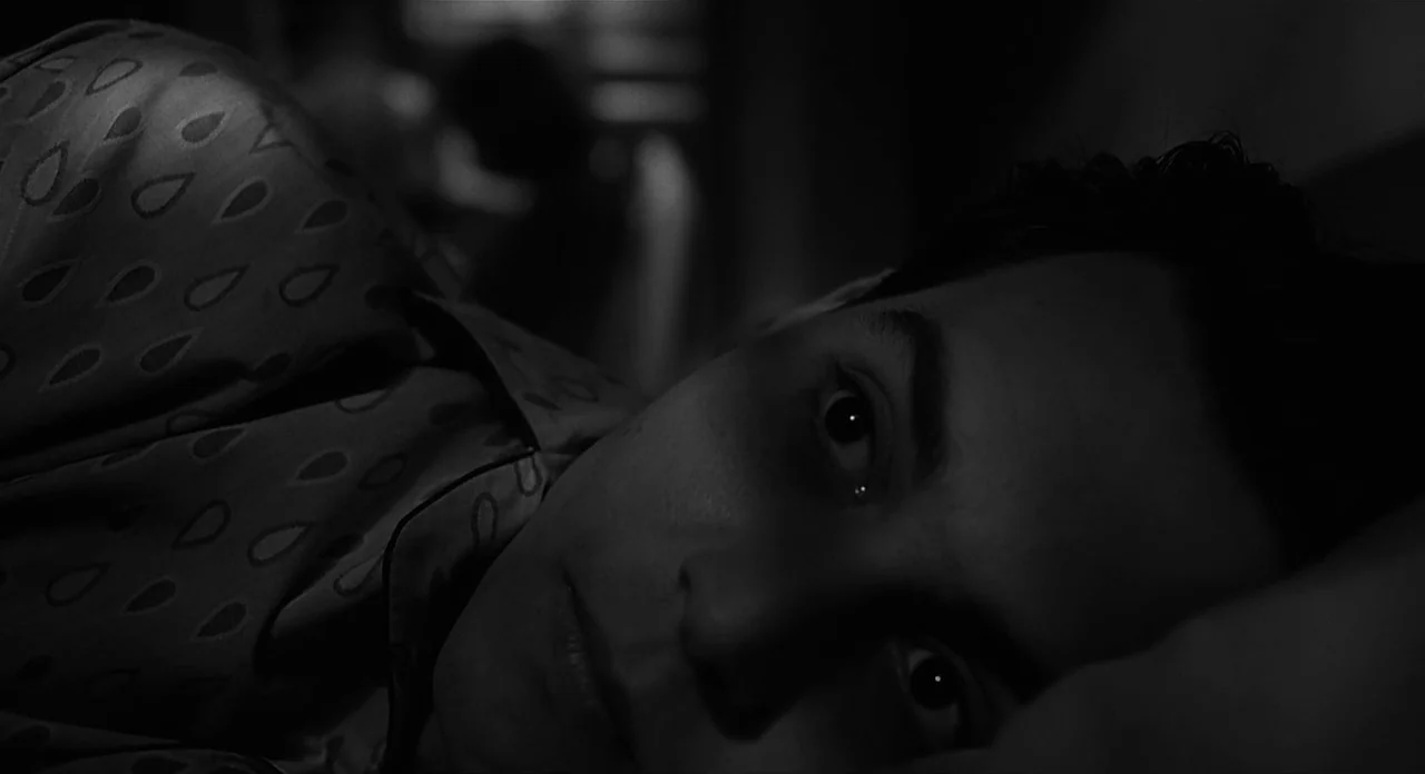 Ed Wood (1994) movie still: closeup — A dimly lit room in black and white with a person lying in bed. A man in patterned pajamas rests his head on a…
