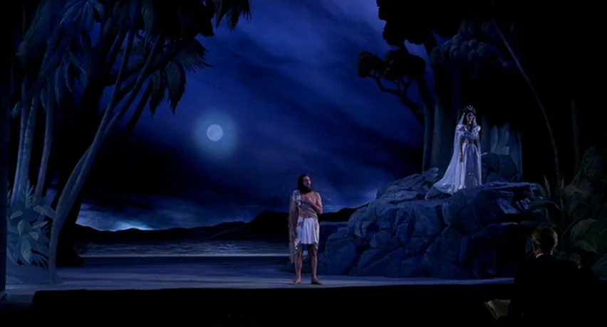 The Man Who Cried (2000) movie still: wide — A theatrical stage set depicts a stylized night landscape with painted palm trees. A man in a tunic…