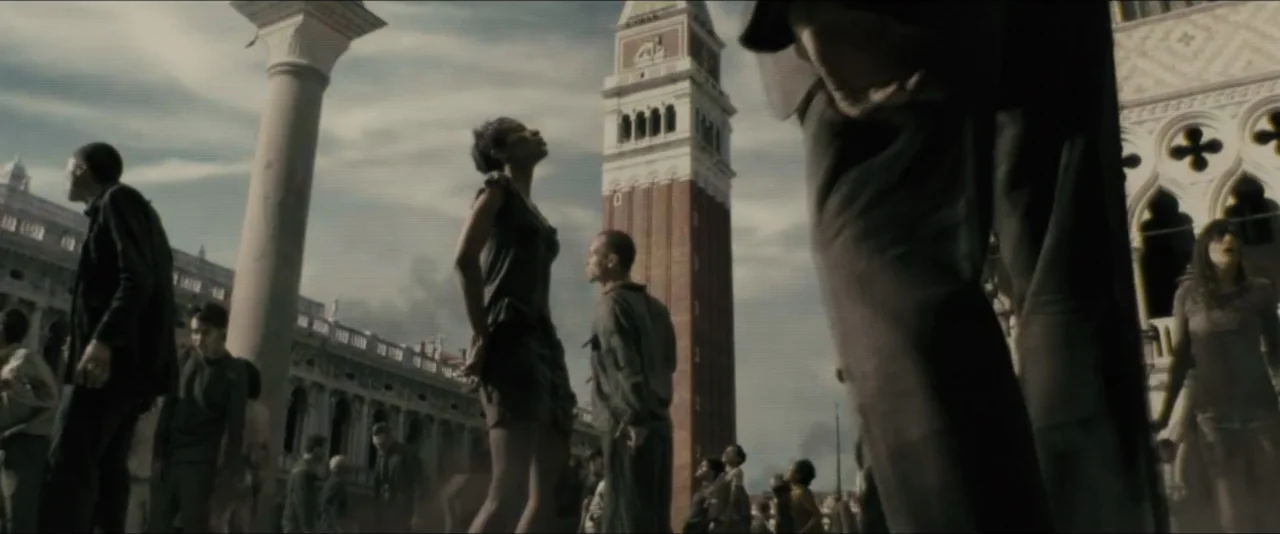 World War Z (2013) movie still: wide — A crowded public square in Venice features stone columns and a tall bell tower. Numerous people stand across…