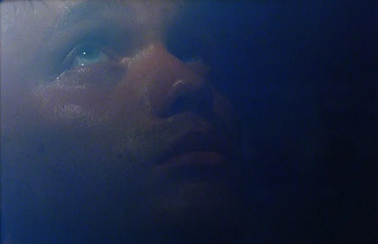 Lili Marleen (1981) movie still: closeup — A man's face emerges from deep darkness in a dimly lit environment. He looks upward with wide,…