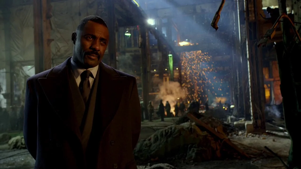 Pacific Rim (2013) movie still: medium — A man stands in the foreground of a dark, ruined industrial structure. Debris and glowing sparks from a…