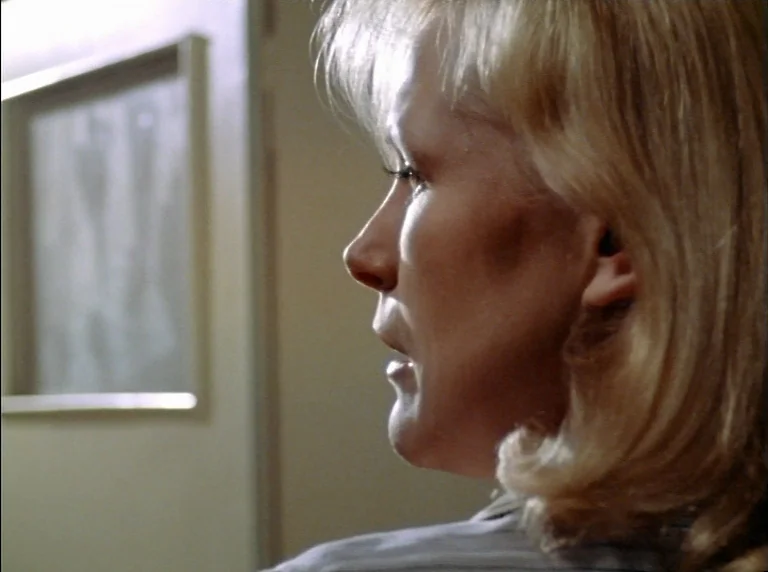 Fear Of Fear (1975) movie still: closeup — An interior space with a beige wall and a rectangular framed glass window. A woman with blonde hair…