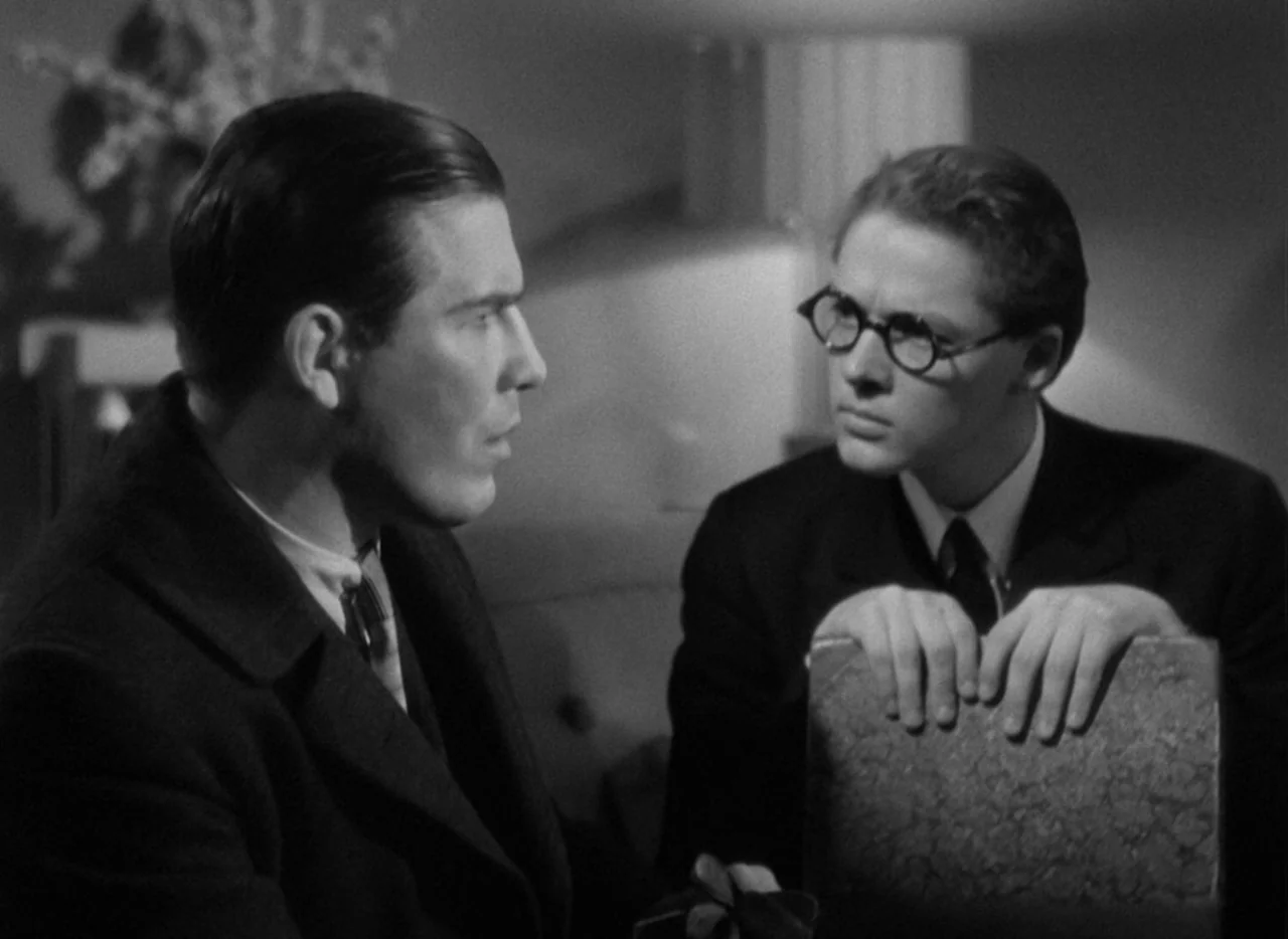 The Thin Man (1934) movie still: medium — Two men sit across from each other in a dimly lit, shadow-filled room. One man leans forward with his…