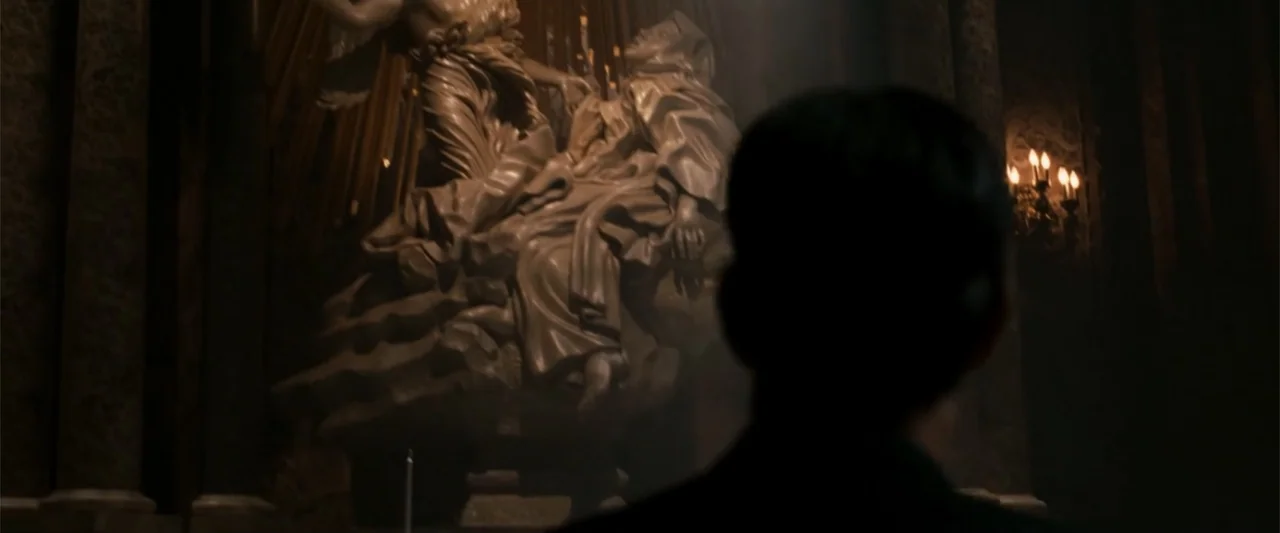 Angels & Demons (2009) movie still: medium — A dark church interior features an ornate marble sculpture illuminated by soft candlelight. A man seen…