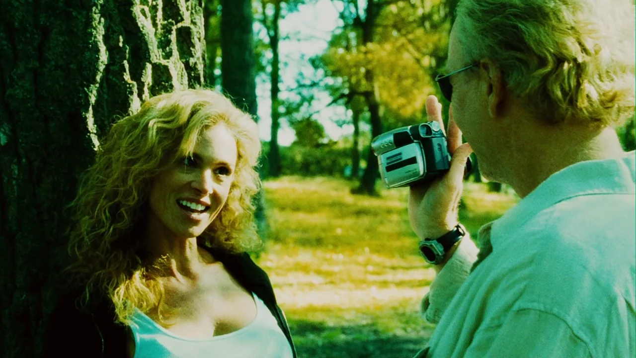Saw III (2006) movie still: medium — A man uses a portable camcorder to record a woman standing by a tree. Sunlit trees and foliage fill the outdoor…