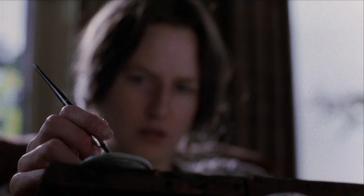 The Hours (2002) movie still: closeup — A dimly lit indoor study features soft, diffused daylight filtering from the background. A woman holds a…