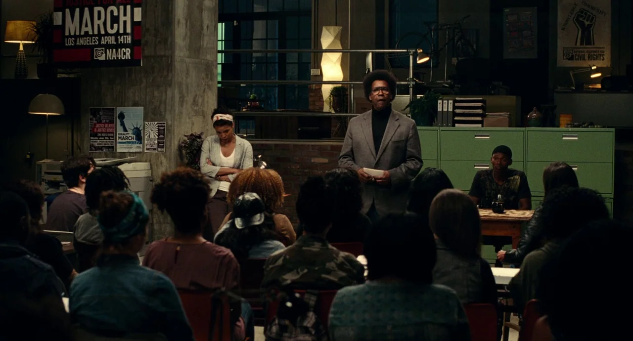 Roman J. Israel, Esq. (2017) movie still: wide — A community meeting space features green filing cabinets, posters on the walls, and chairs. A man…