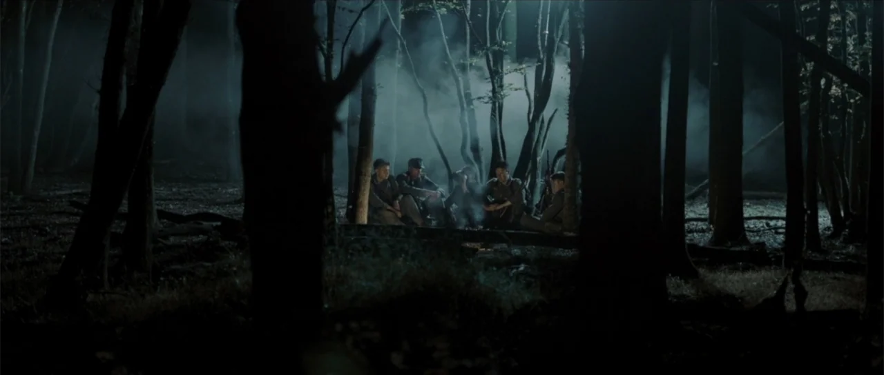 Sin retorno (2009) movie still: wide — A dense, fog-filled patch of woods at night featuring a small, dim campfire. A group of soldiers in uniform…