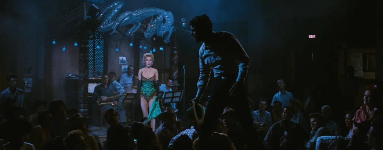 Bus Stop (1956) movie still: wide — A dark, crowded nightclub features a performance stage with a glowing dragon-shaped neon sign. A woman stands…
