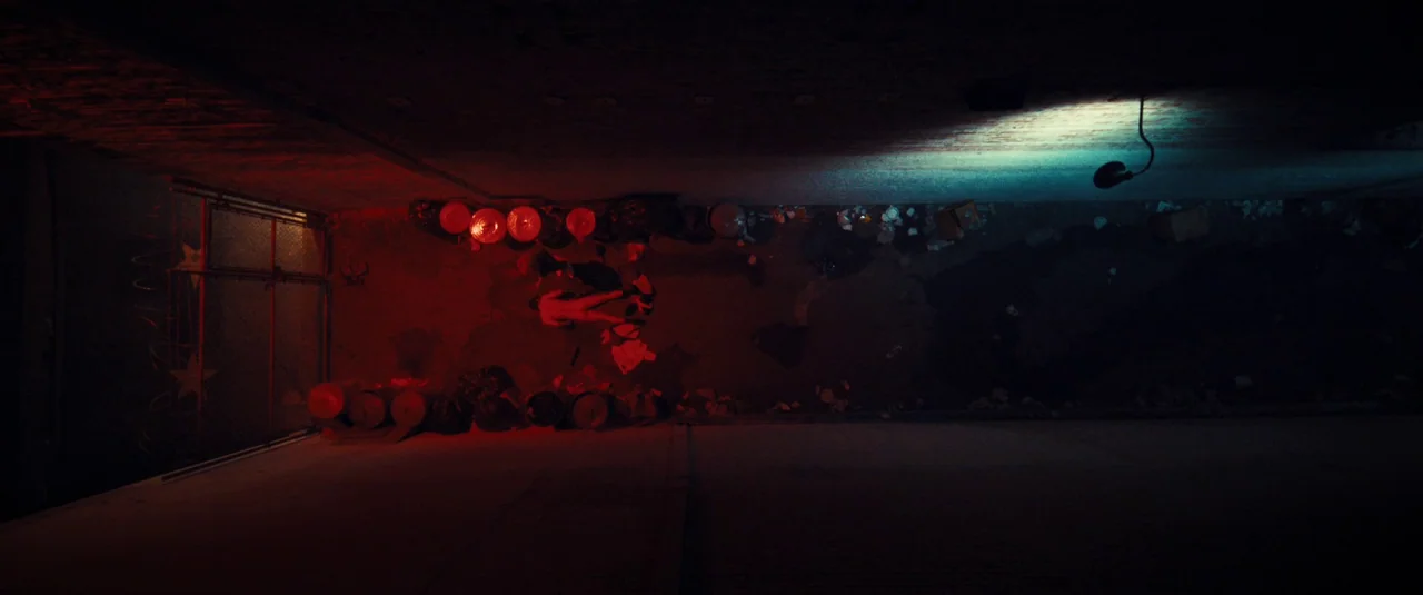 MaXXXine (2024) movie still: establishing — A dark narrow urban passage filled with trash bags and scattered refuse. The space is illuminated by a…