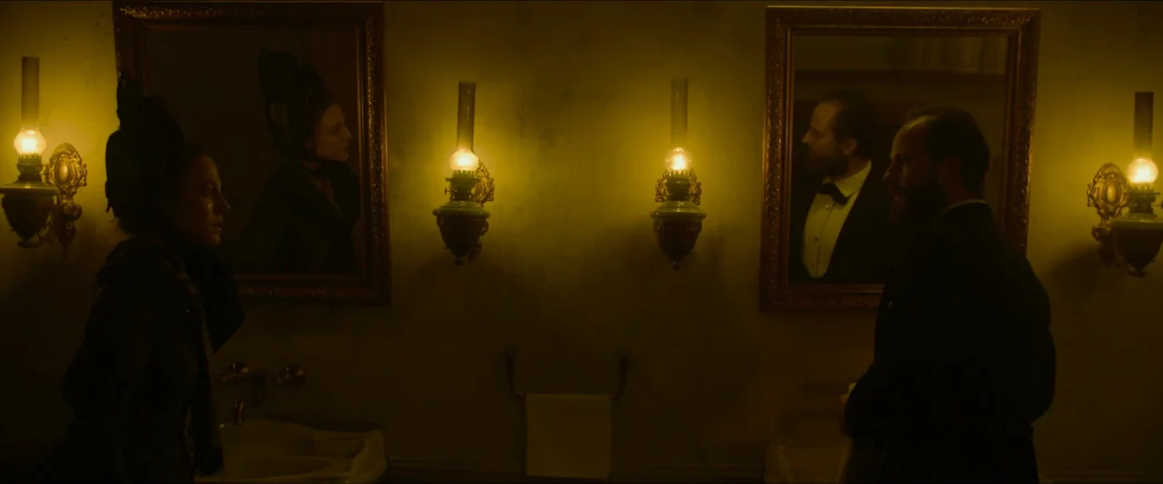 Tchaikovsky’s Wife (2022) movie still: medium — A dimly lit period washroom features two ornate mirrors mounted on a wall. A man and woman stand…